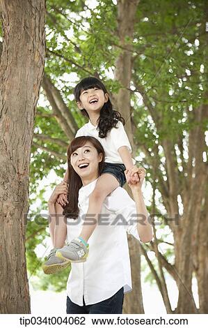 Stock Image - a daughter on mother's shoulders in forest . Fotosearch