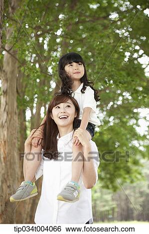 Stock Photograph - a daughter on mother's shoulders in forest . Fotosearch