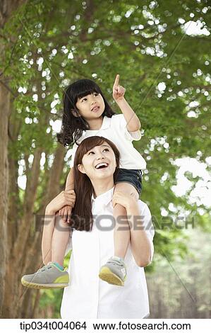 a daughter pointing somewhere while sitting on mother's shoulders View Large Photo Image Picture - a daughter pointing somewhere while sitting on mother's shoulders. Fotosearch