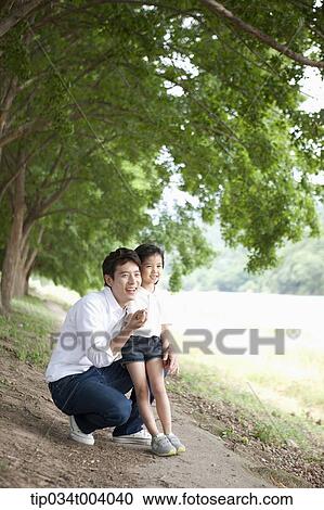 Stock Image - a daughter pointing somewhere while having a rest next to a field with a father. Fotosearch