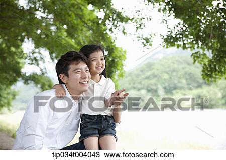 Stock Image - a daughter pointing somewhere while having a rest next to a field with a father. Fotosearch