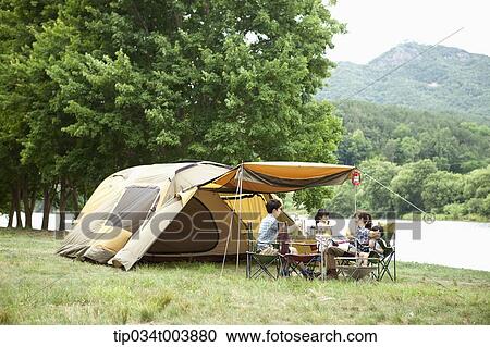 Stock Image - a family in camping place having a meal next to a lake . Fotosearch