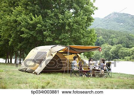 Stock Image - a family in camping place having a meal next to a lake . Fotosearch