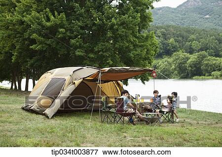 Stock Photo - a family in camping place having a meal next to a lake . Fotosearch