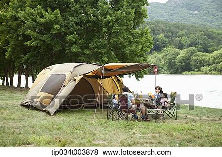 Stock Photo - a family in camping place having a meal next to a lake . Fotosearch