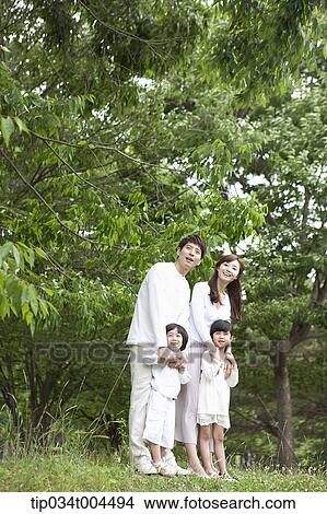 Picture - a family posing on grass with trees behind them . Fotosearch