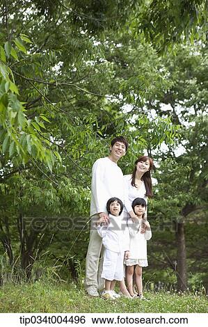 Stock Photograph - a family posing on grass with trees behind them . Fotosearch