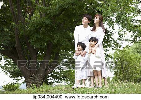 Stock Image - a family standing on grass with a big tree next to them. Fotosearch
