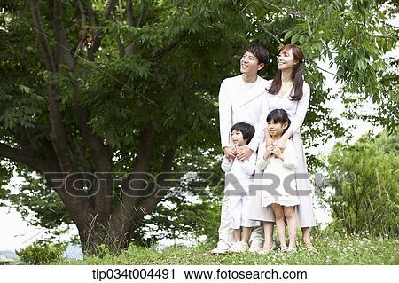 Stock Image - a family standing on grass with a big tree next to them. Fotosearch