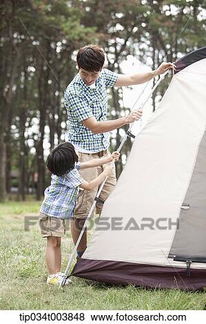 Stock Photo - a father and son building a tent in camping place. Fotosearch