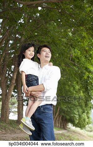 Picture - a father holding a daughter in front of trees . Fotosearch