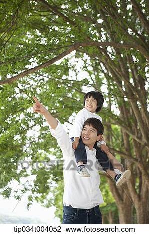 Stock Image - a father pointing somewhere while holding a son on his shoulders . Fotosearch
