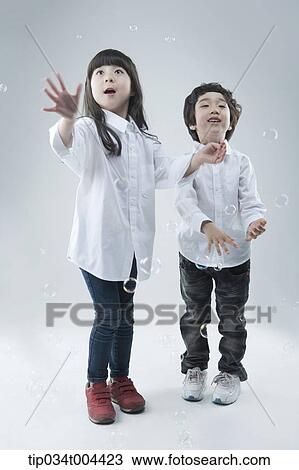 Stock Image - a female and a male kids playing with bubbles . Fotosearch