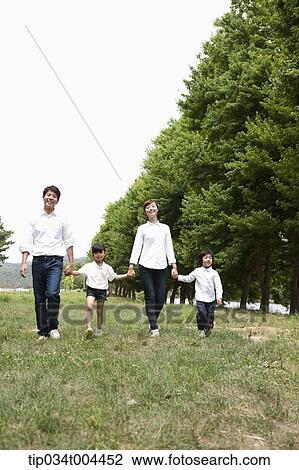 Stock Image - a female kid and parents walking hand in hand on grass . Fotosearch