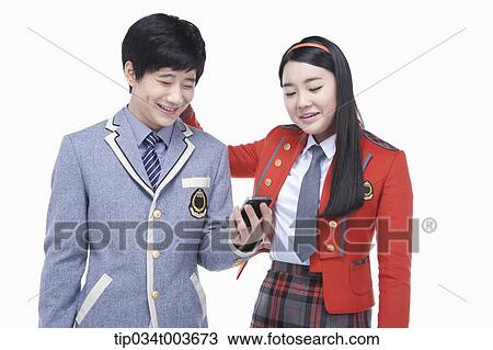 Stock Image - a female student hitting male student's neck while reading his smartphone screen . Fotosearch