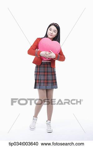 Stock Image - a female student holding a pink heart cushion in her arms. Fotosearch