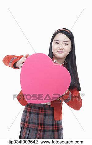 Stock Image - a female student holding a pink heart cushion smiling. Fotosearch