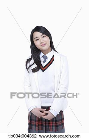 Stock Image - a female student in school uniform wearing a white jacket standing with her hands together. Fotosearch