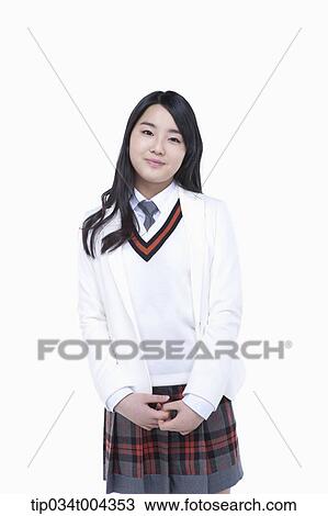 Stock Image - a female student in school uniform wearing a white jacket standing with her hands together. Fotosearch