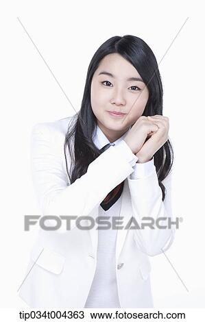Stock Image - a female student in school uniform standing with hands together next to her cheek . Fotosearch