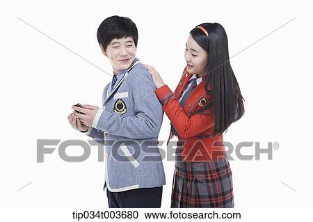 Stock Image - a female student looking at male student's smartphone over his shoulders. Fotosearch