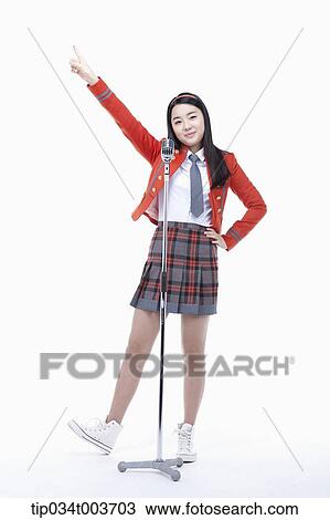 Stock Image - a female student pointing with a hand while standing behind a microphone stand . Fotosearch
