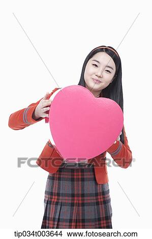 Picture - a female student posing with a pink heart cushion. Fotosearch