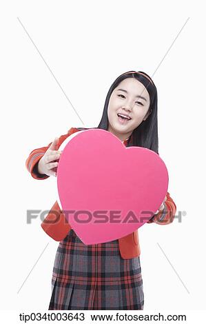Stock Image - a female student posing with a pink heart cushion. Fotosearch