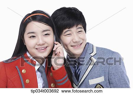 Stock Image - a female student talking on a mobile phone while male student tries to overhear. Fotosearch