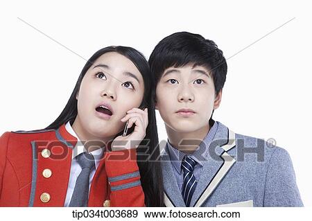 Stock Photo - a female student talking on a mobile phone while male student tries to overhear. Fotosearch
