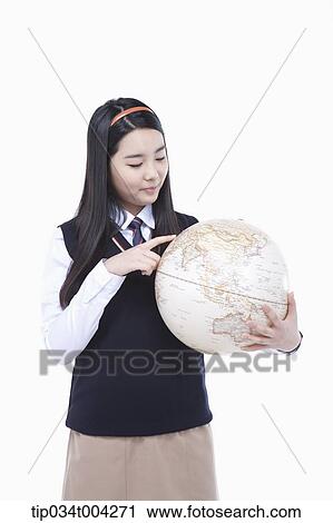 Stock Image - a female student wearing school uniform looking at a globe . Fotosearch