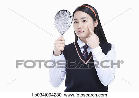 Stock Image - a female student wearing school uniform looking at herself through a mirror. Fotosearch