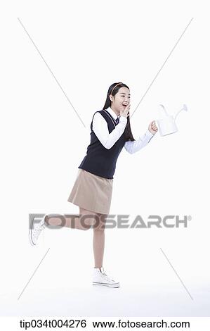 Stock Photograph - a female student wearing school uniform running with a garden kettle. Fotosearch