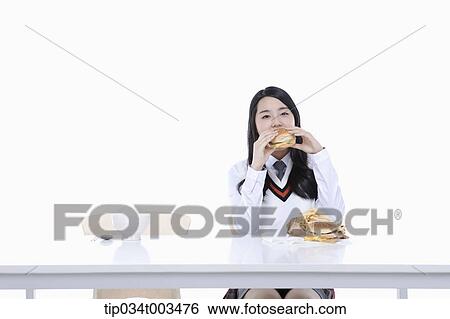 Stock Photograph - a female student with school uniform biting a burger . Fotosearch