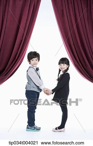 Stock Image - a girl and a boy facing each other hands in hands while looking at audience. Fotosearch