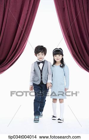 Picture - a girl and a boy hand in hand standing on a stage with red curtains . Fotosearch