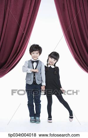 Stock Photo - a girl and a boy hand in hand standing on a stage with red curtains . Fotosearch