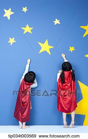 Stock Photo - a girl and a boy posing like a superman in their backs while wearing red capes. Fotosearch