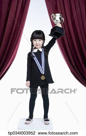 a girl holding a trophy cup on a stage with red curtains View Large Photo Image Stock Image - a girl holding a trophy cup on a stage with red curtains. Fotosearch