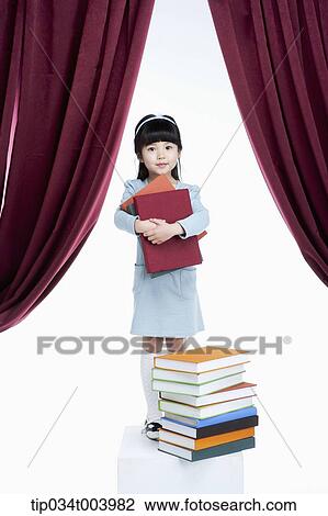 a girl holding books while standing in front of pile of books on a stage View Large Photo Image Stock Image - a girl holding books while standing in front of pile of books on a stage. Fotosearch