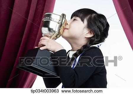Stock Image - a girl kissing her trophy cup in front of red curtains. Fotosearch