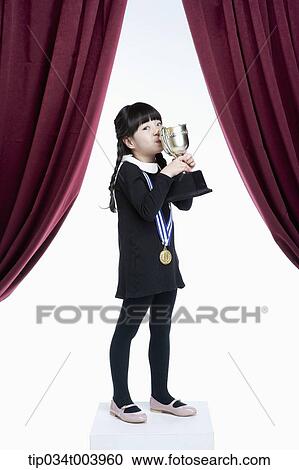 Stock Image - a girl kissing her trophy cup on a stage with red curtains. Fotosearch