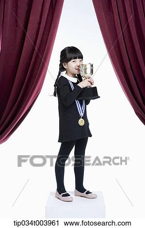 Stock Image - a girl kissing her trophy cup on a stage with red curtains. Fotosearch