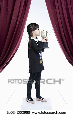 Stock Photo - a girl kissing her trophy cup on a stage with red curtains. Fotosearch