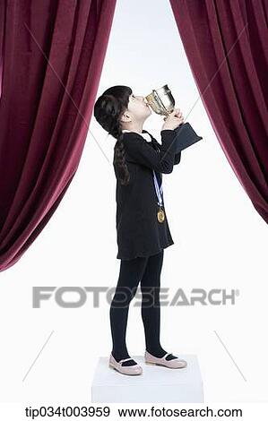 Stock Photo - a girl kissing her trophy cup on a stage with red curtains. Fotosearch