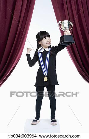 Picture - a girl posing with a trophy cup on a stage with red curtains. Fotosearch