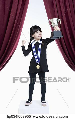 Stock Photography - a girl posing with a trophy cup on a stage with red curtains. Fotosearch