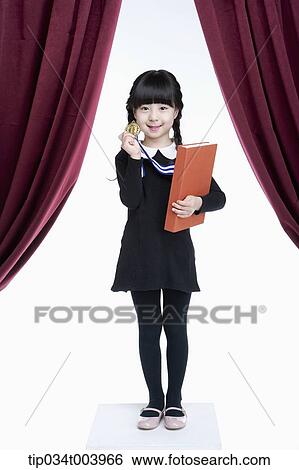 Stock Photograph - a girl wearing a medal holding a book in her arm . Fotosearch