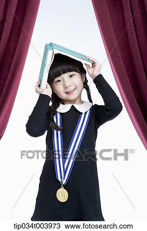 Stock Image - a girl wearing a medal putting a open book on her head . Fotosearch