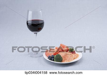 Stock Photo - a glass of red wine and a plate of salmon with vegetables and fruits. Fotosearch
